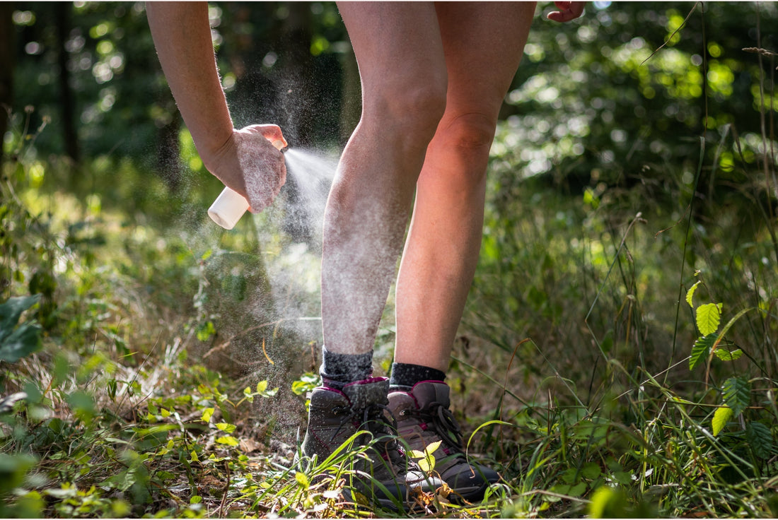 A person standing in grass field while spraying cleaning solution on their shoes.